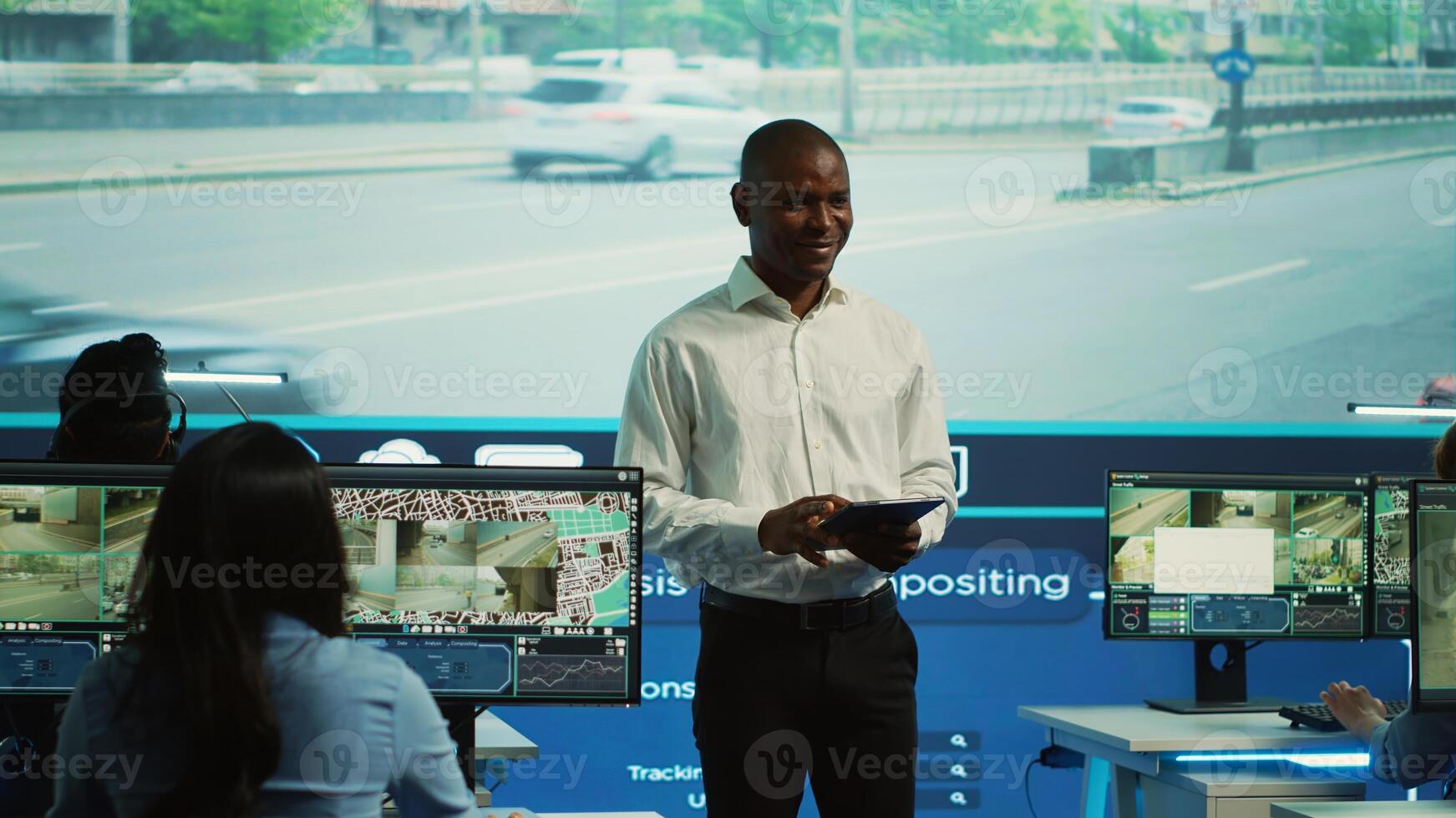 Team leader supervising his team in control center office to work on monitoring traffic by following real time surveillance . Diverse agency employees examining city streets via CCTV. Camera A. photo
