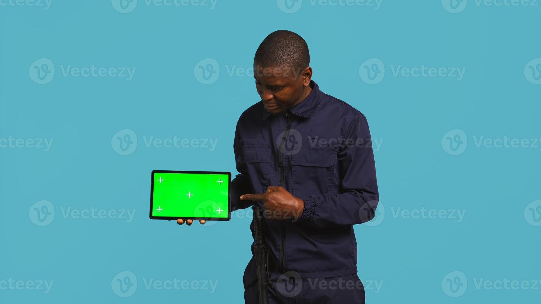 Portrait of security agent presenting chroma key tablet and securing assigned post, studio background. Guardian points finger to isolated screen device while handling security breaches, camera B photo