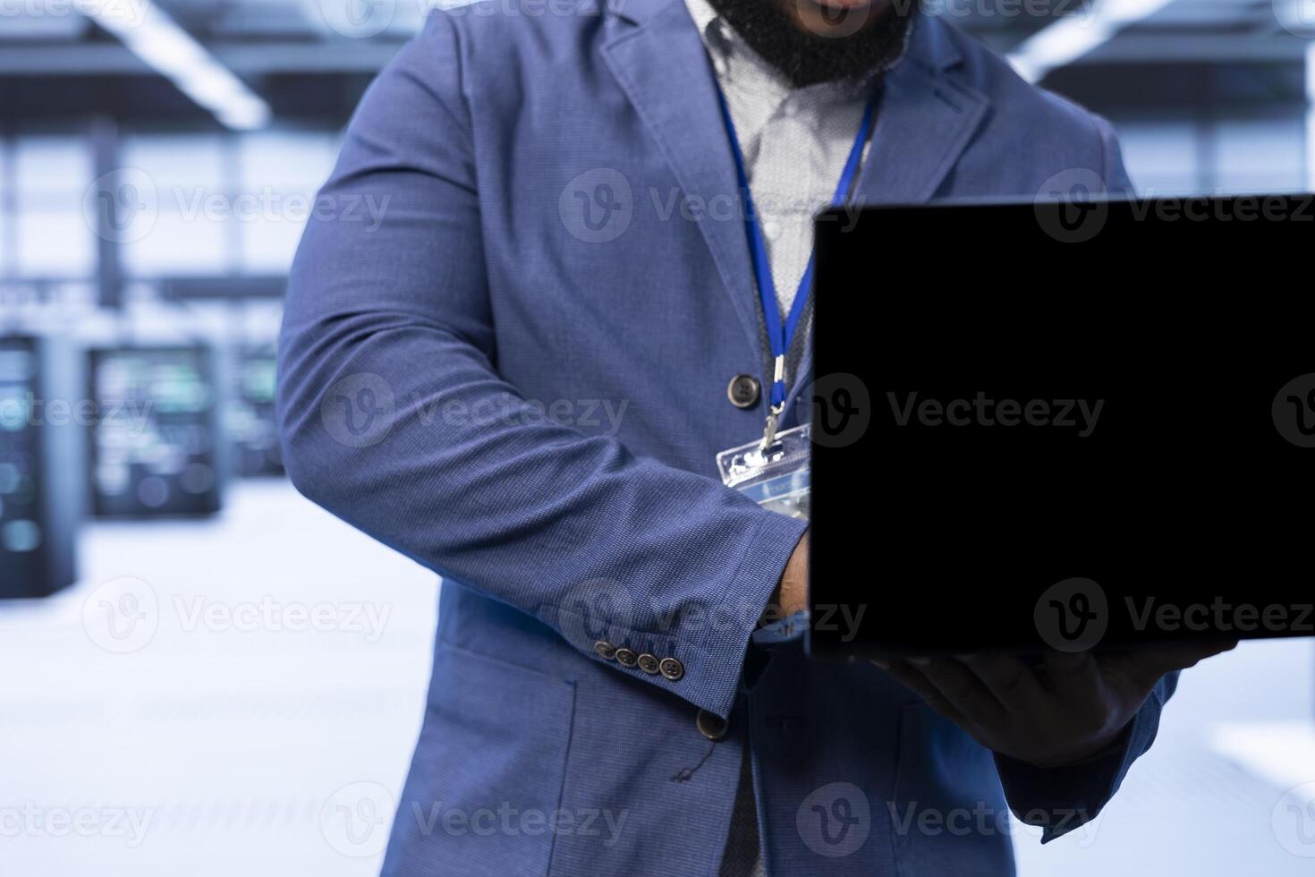 Admin walking in data center, using laptop to configure network infrastructure such as routers, switches and firewalls. Close up of IT expert in server hub looking for technical issues using notebook photo