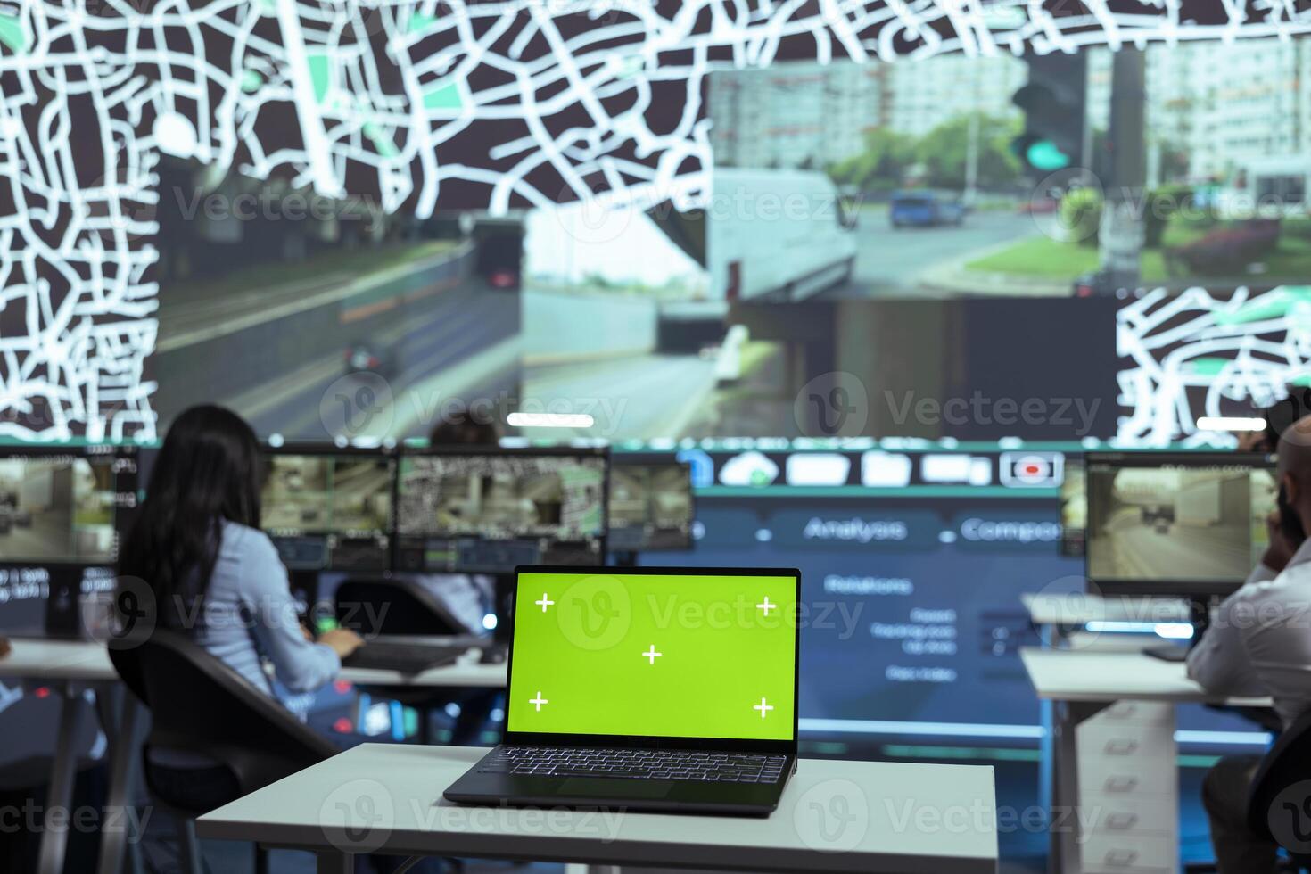 Agency employees look at satellite map and CCTV footage in monitoring room, working with greenscreen display. People following delivery trucks in the city and gives directions for shipment location. photo