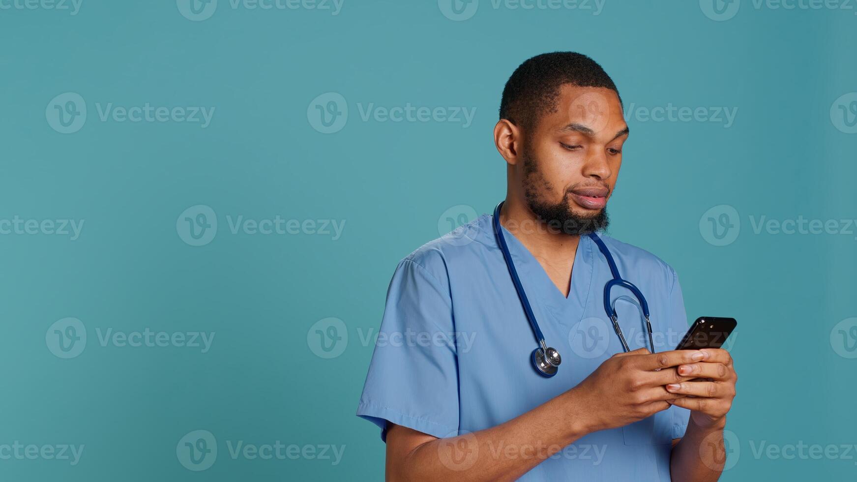Male nurse using mobile phone to scroll on social media feed during hospital job shift break. Healthcare worker using smartphone to text friends, studio backdrop, camera A photo