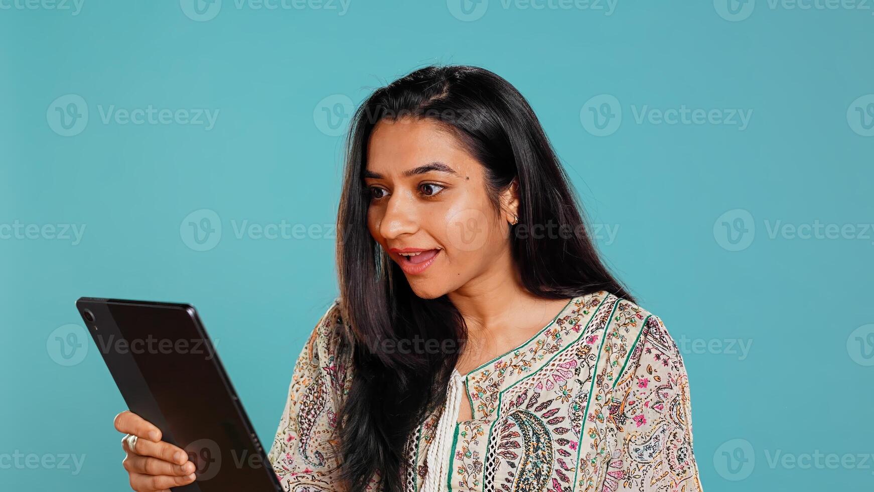 Cheerful woman gossiping with friends during videoconference meeting using tablet, studio background. Jolly person bonding with mates, spreading rumors during online videocall on device, camera B photo