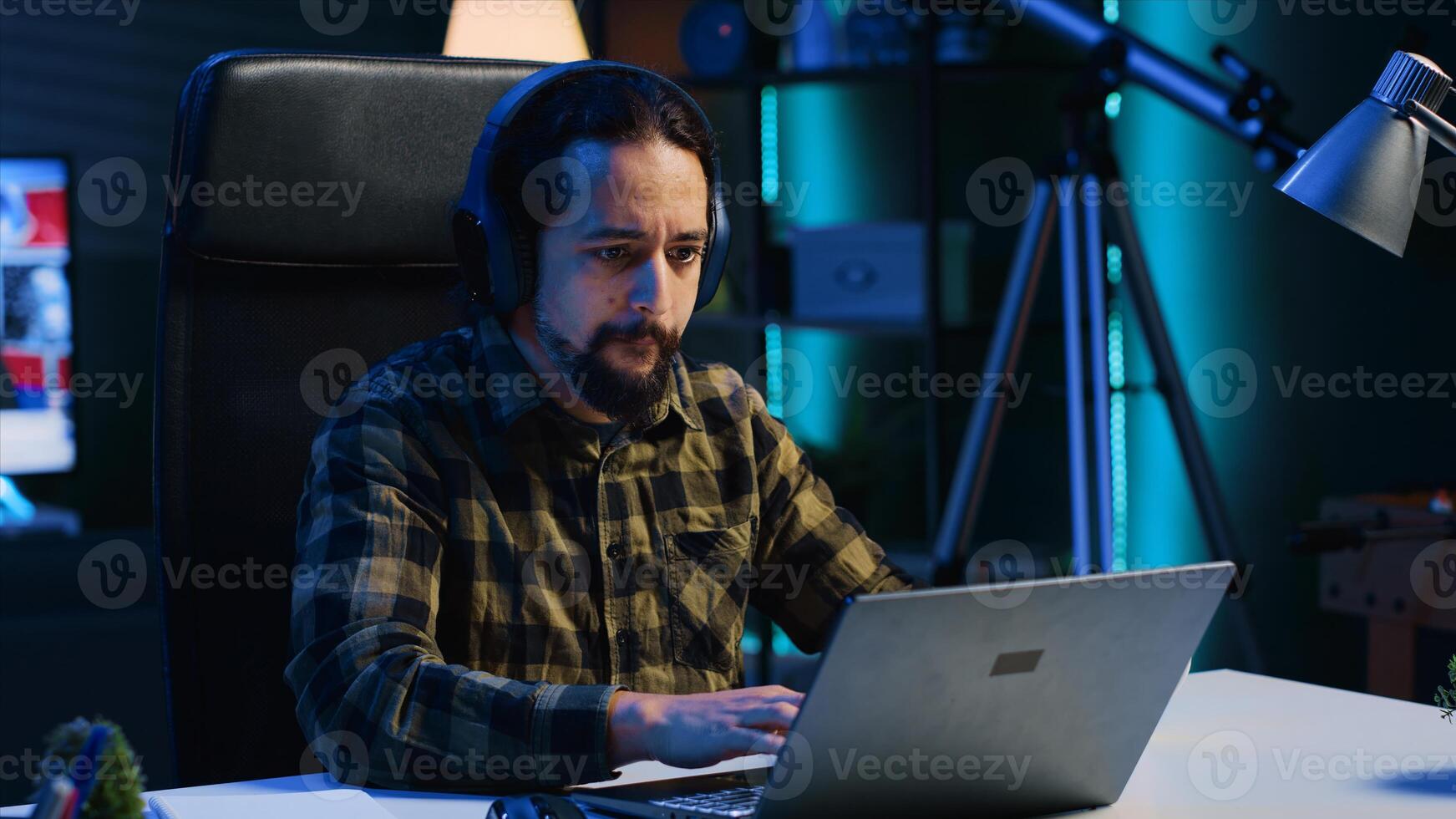 Remote employee with wireless headphones working from living room office, sending emails. Freelancer doing internet research using laptop while listening to music to make time pass faster photo
