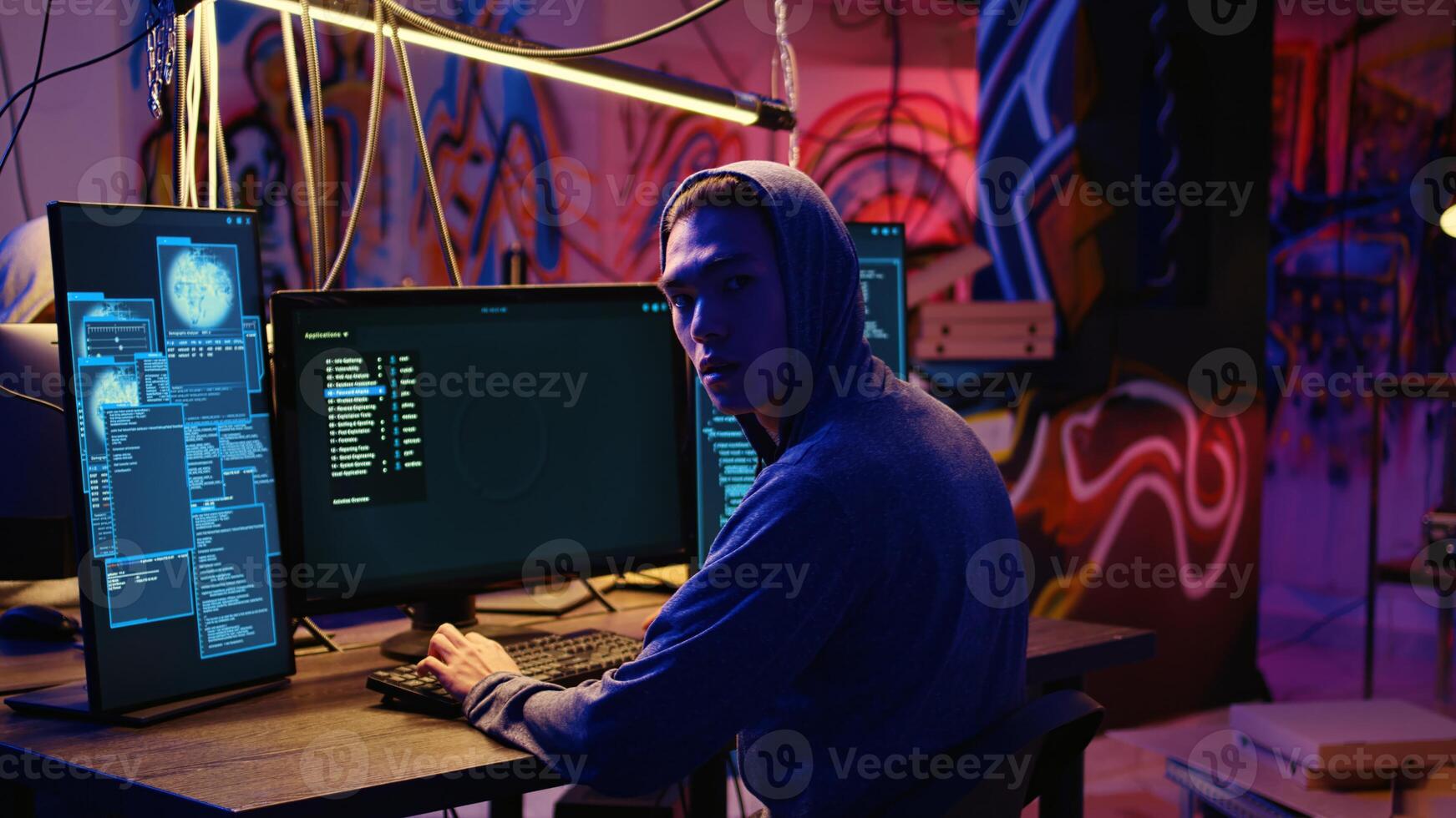 Asian hacker hiding in underground bunker, looking over his shoulder and feeling anxious after stealing data from victims using computer virus, scared about being caught by police photo