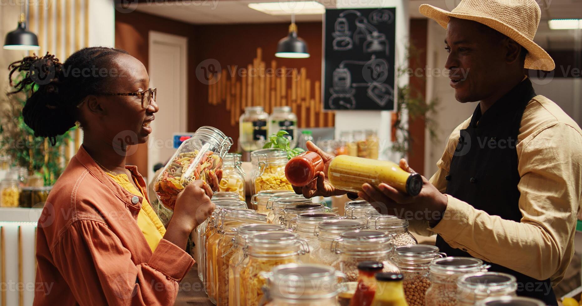 Merchant presenting additives free homemade sauces for tasty meals, recommending ethically sourced pantry supplies and pasta. Seller promoting his organic bulk products in glass jars. Camera 2. photo