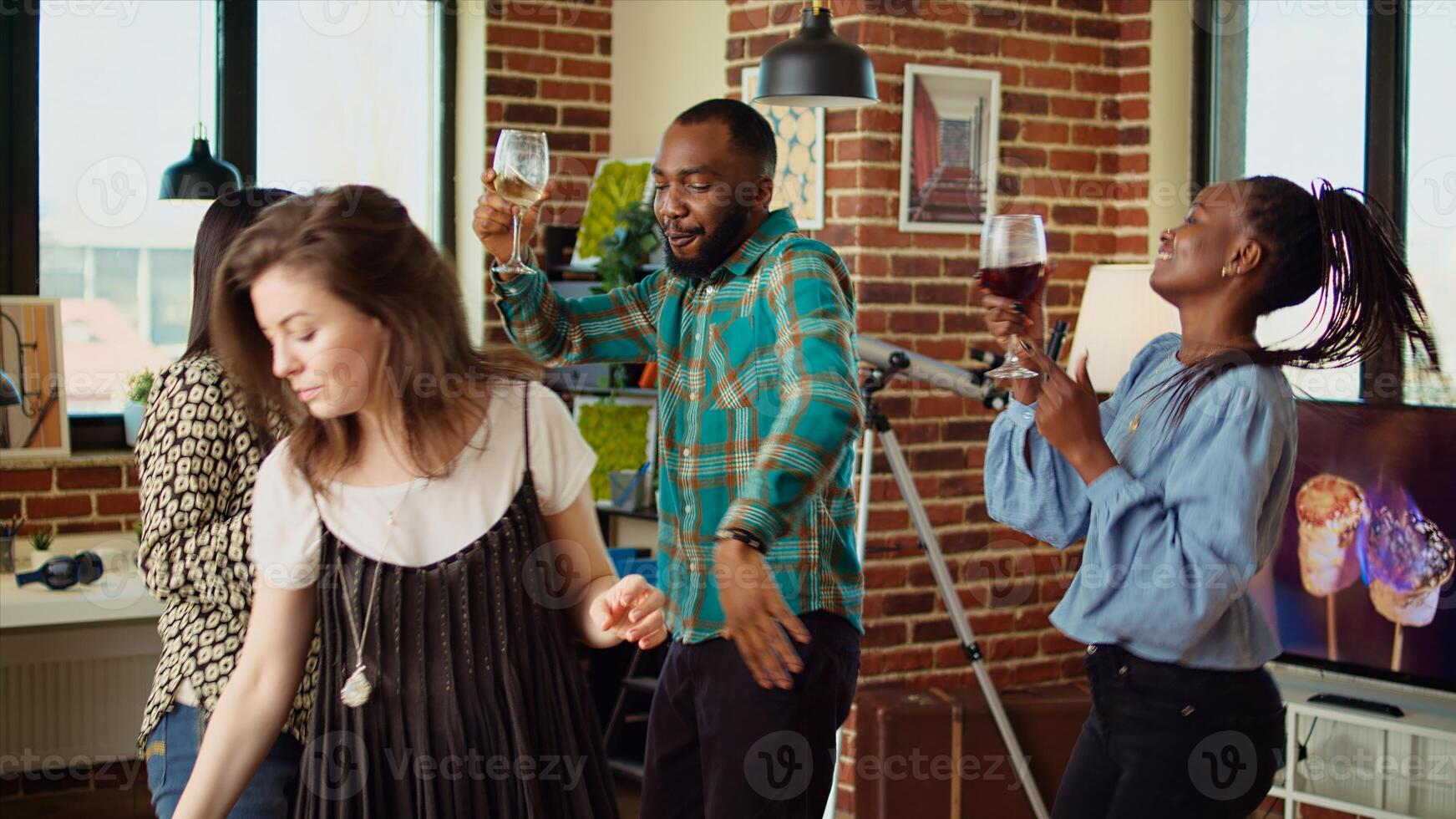 Diverse mix of guests at home party sharing laughter and dance moves in living room, holding wine glasses in hand. Smiling friends dancing on lively beats during weekend hangout, shaking hips photo