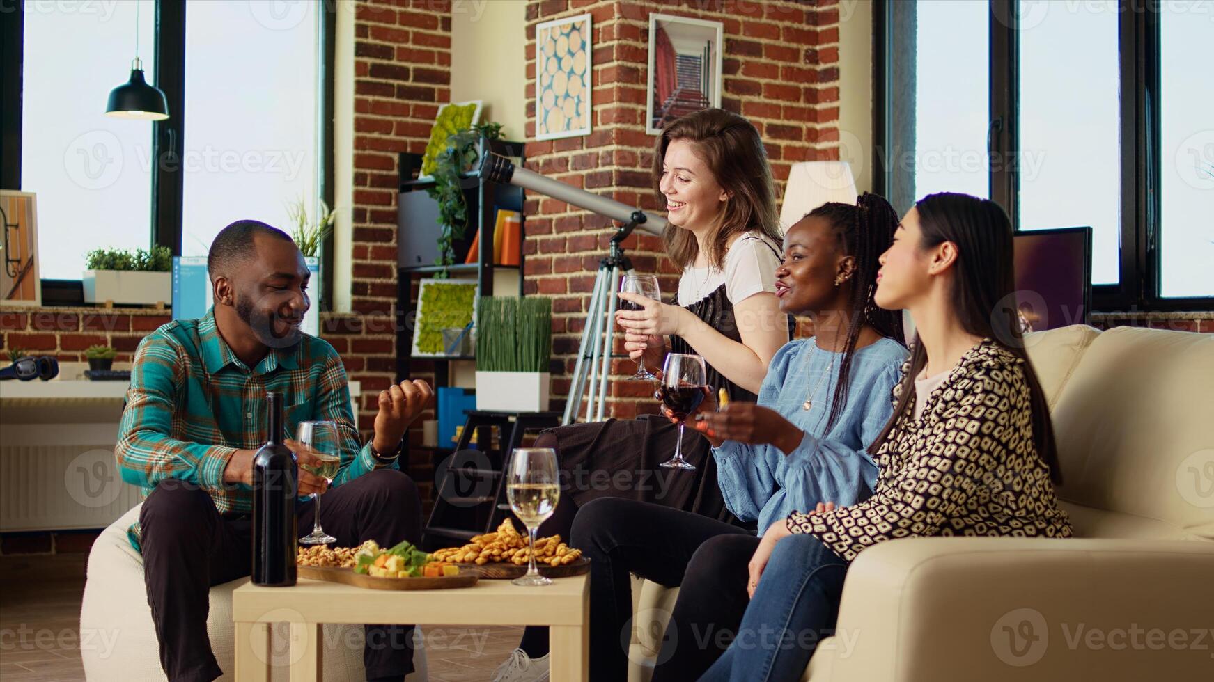 Culturally diverse friends talking, conversing with each other, drinking wine, tasting cheese and bread sticks at reunion gathering. Multicultural mates enjoying social life in cozy living room photo