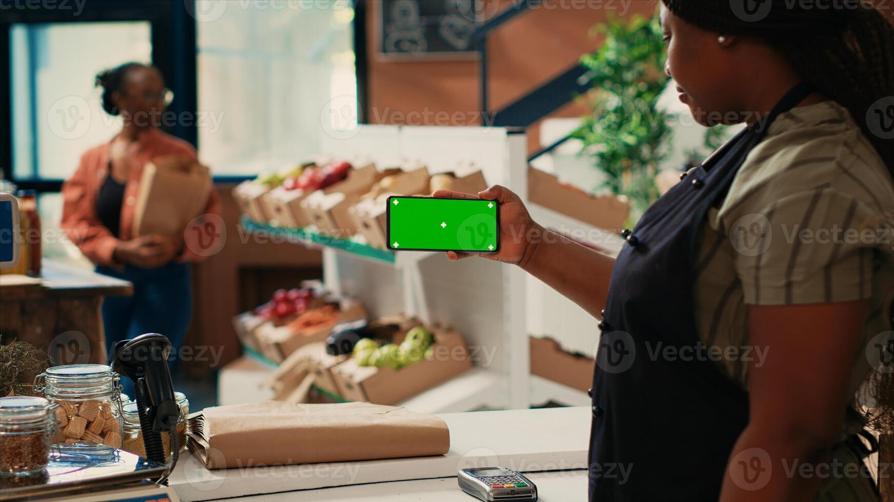 African american vendor using greenscreen template at counter, presenting chromakey display on smartphone. Woman seller holding phone with isolated mockup layout and copyspace. photo