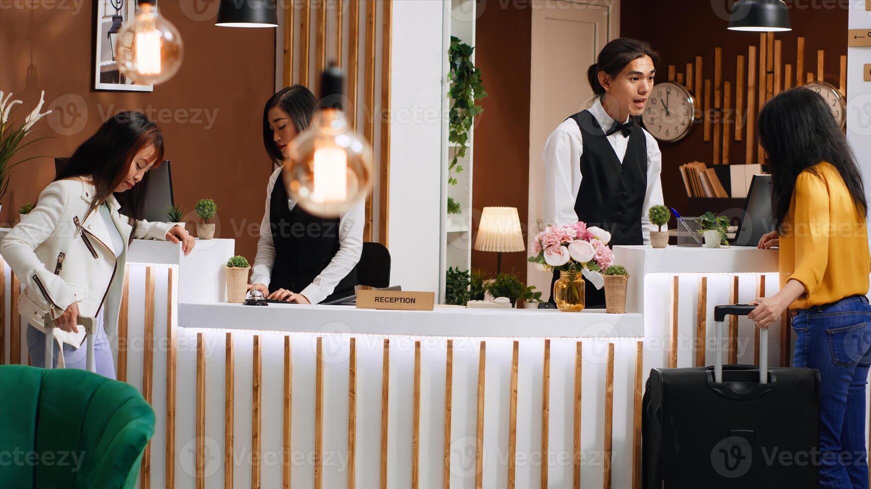 Young customer approaching front desk in hotel lobby, preparing for check in process after long flight. Asian staff greeting guest at reception, discussing about room reservation and facilities. photo