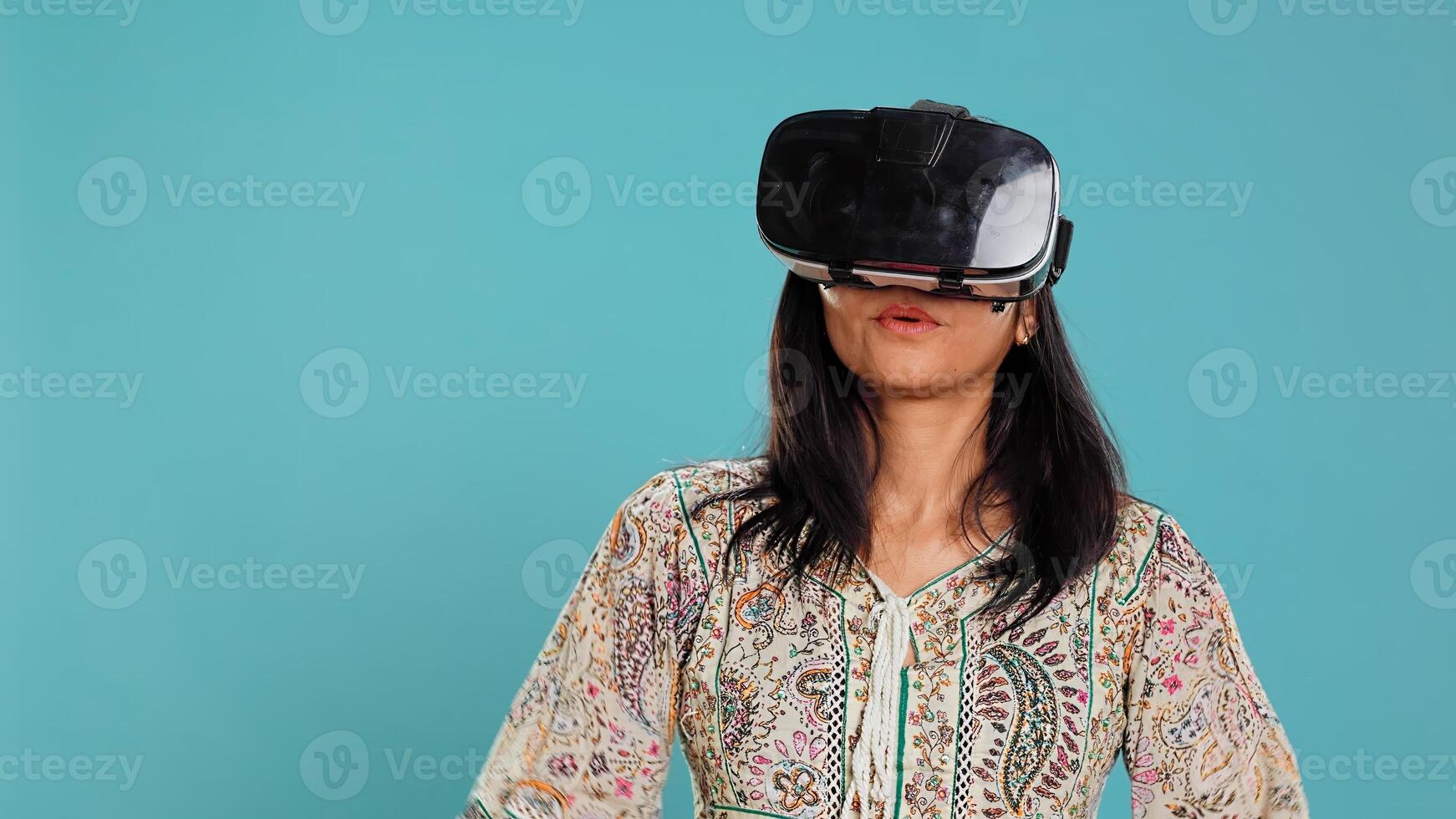 Indian woman wearing virtual reality headset, doing swiping gestures. Technology enthusiast using high tech futuristic modern VR gadget, isolated over studio background, camera B photo