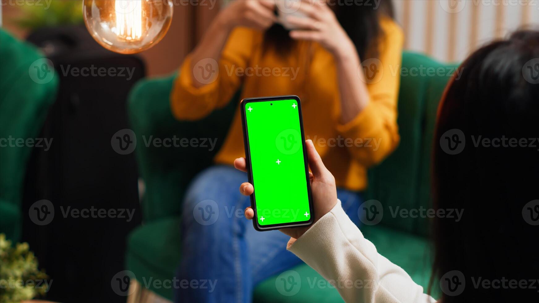 Woman checking greenscreen display on smartphone layout, passing time in lounge area at hotel. Asian tourist sitting on sofa with phone running isolated chromakey template on screen. photo