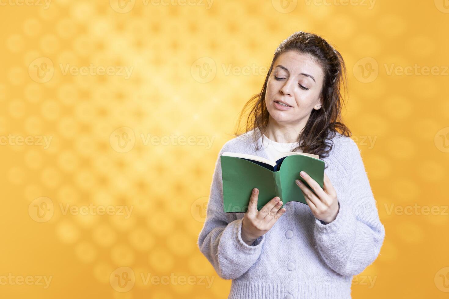Jolly woman turning page on book, enjoying story, conveying joy of reading concept, studio background. Radiant geek reading hardcover novel, showing appreciation for literature photo