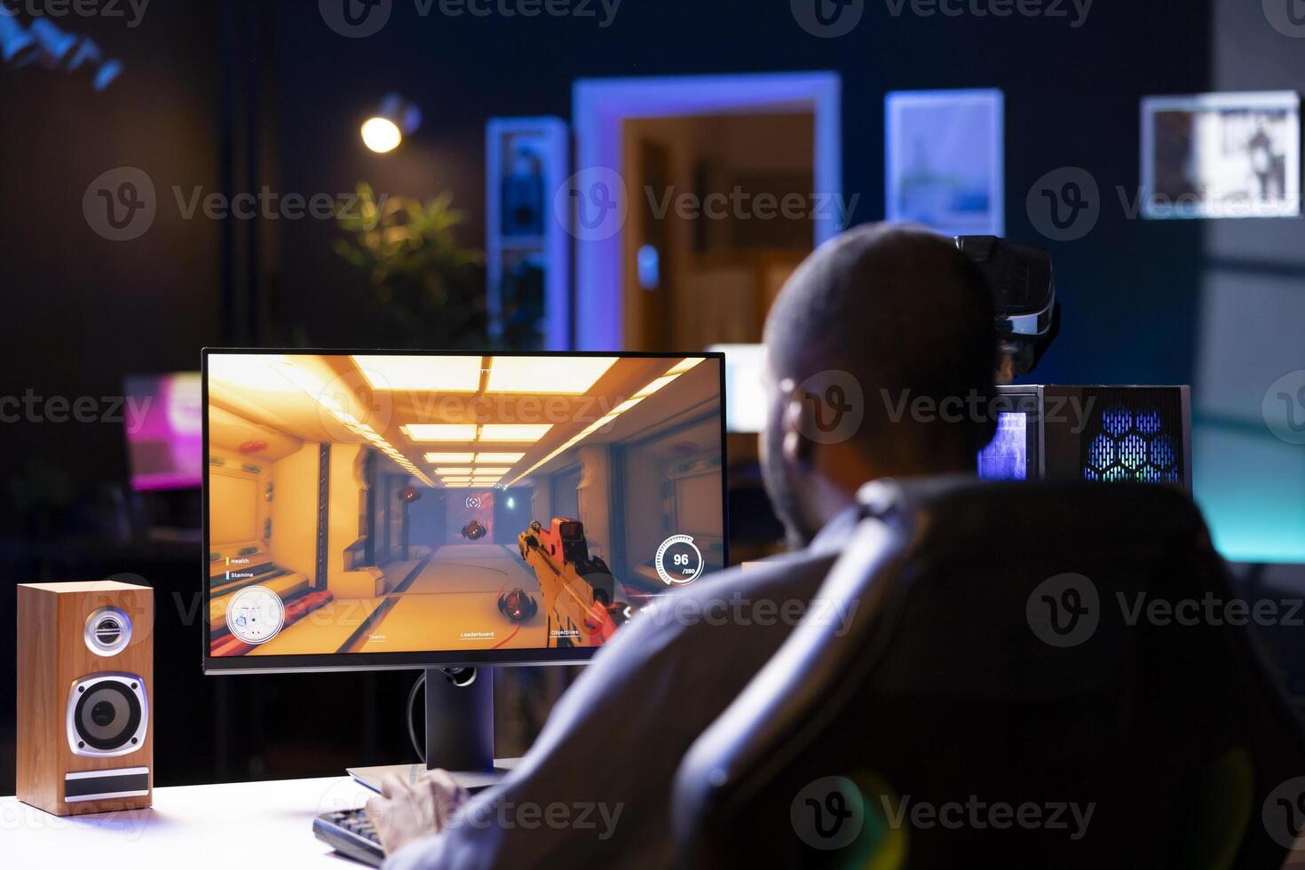 Man in living room playing games on gaming PC at computer desk, enjoying day off from work. Gamer battling enemies in online multiplayer shooter from neon lights ornate home photo