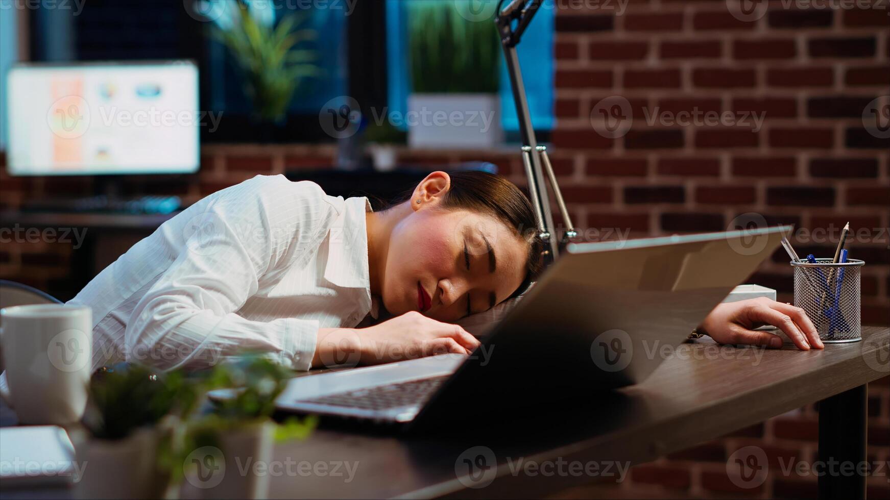 Tired employee sleeping on workspace desk after struggling all night to finish writing emails. Drowsy businesswoman napping in office after working overnight, asleep at laptop, camera B photo