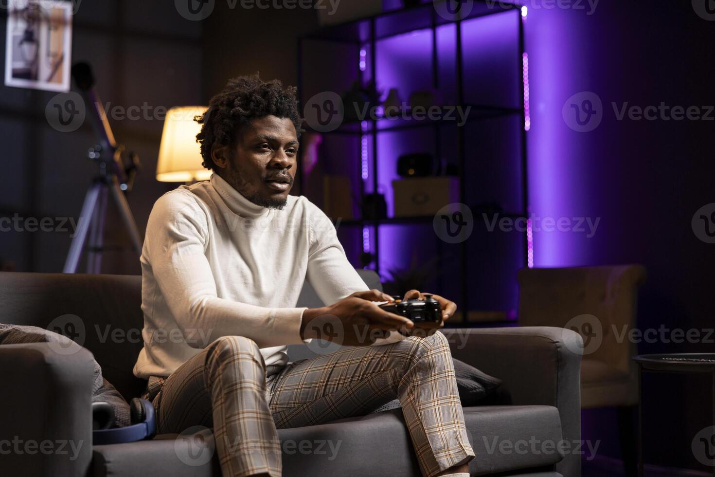 Player playing videogames on console late at night in purple neon lit room, struggling to stay awake. Man using gamepad controller to try and finish game level before going to sleep, feeling sleepy photo