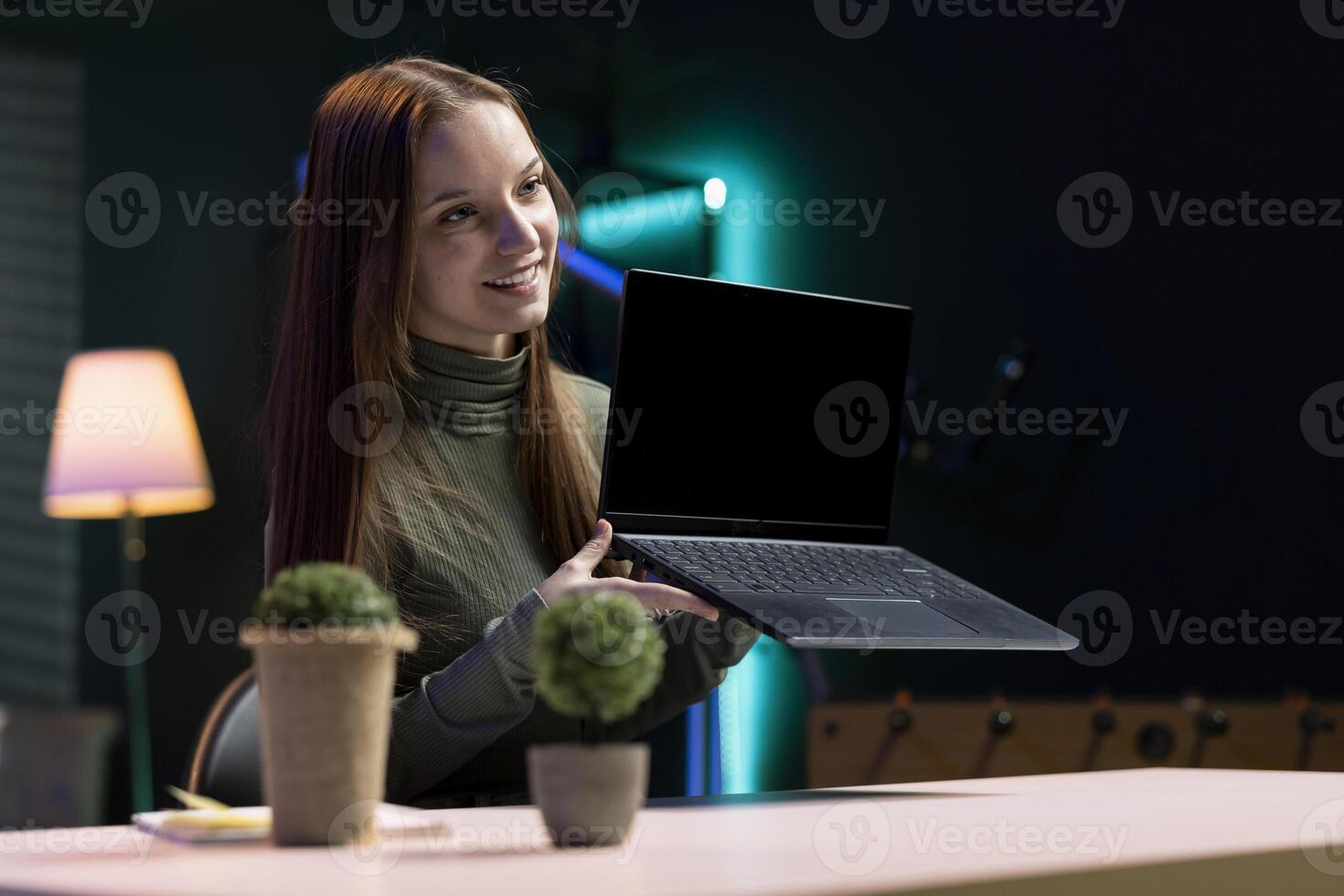 Smiling gen Z online show host filming content about best laptop releases of the year. Cheerful young content creator recording newly launched notebook review in home studio photo