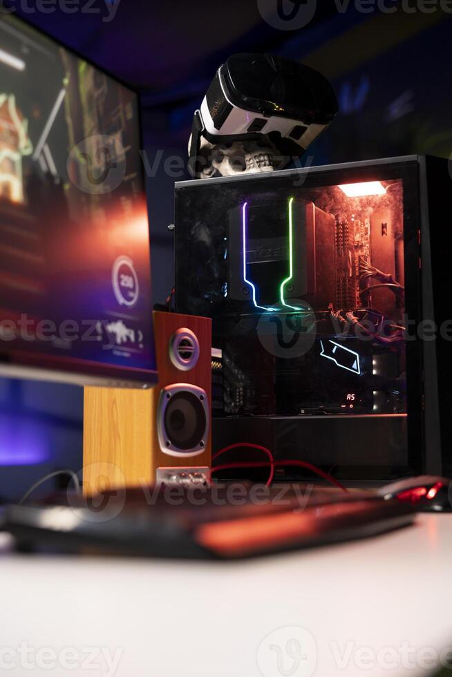 RGB lit parts on opened gaming PC tower next to keyboard, stereo speakers, display and high tech VR headset in empty apartment. Computer with modern hardware, monitor and virtual reality glasses photo