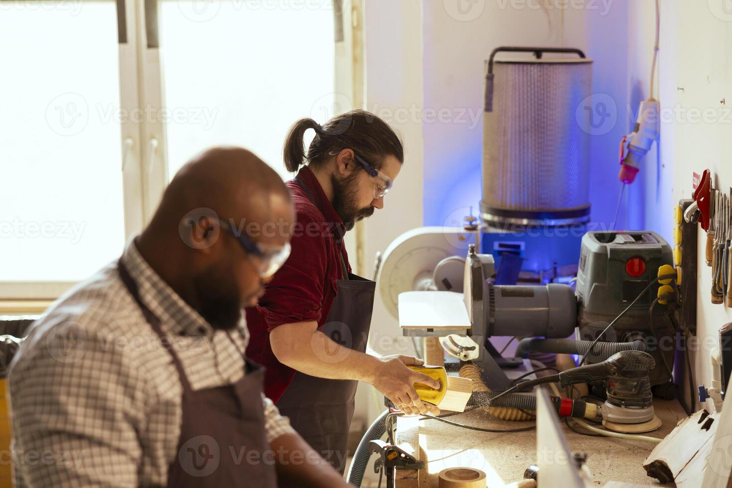 Team of woodworkers in assembly shop using sandpaper for sanding wooden surface before painting it, ensuring adequate finish. Carpenters wearing safety glasses using abrasive sponges photo