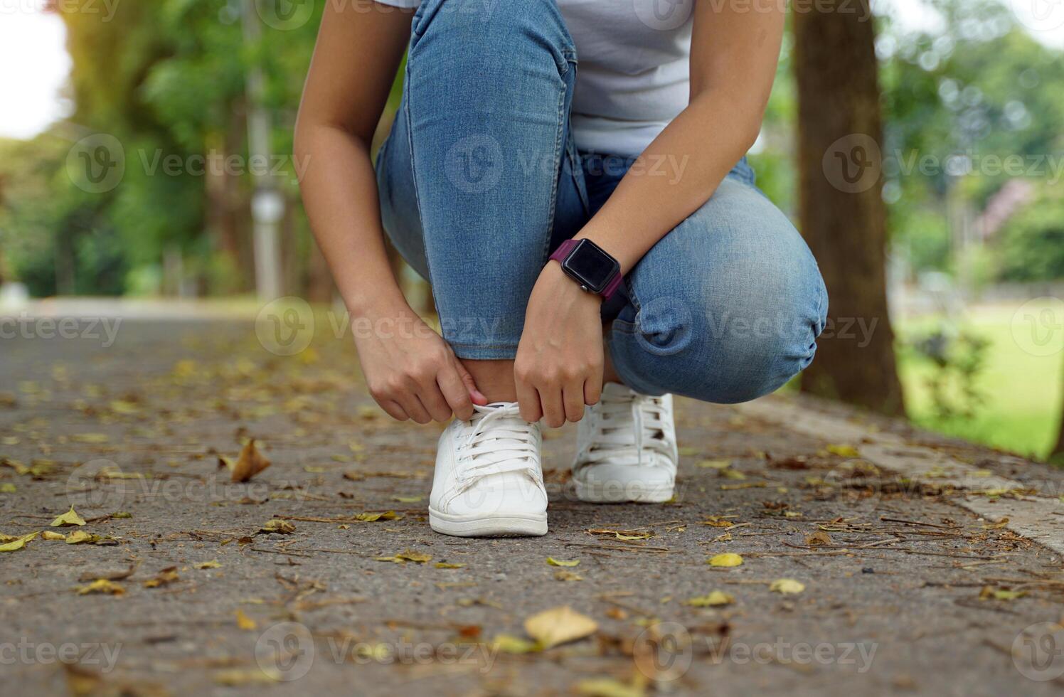 Young Asian woman sits tying the laces of her white sneakers on the street of the park. Her hand is wearing a smart watch. photo