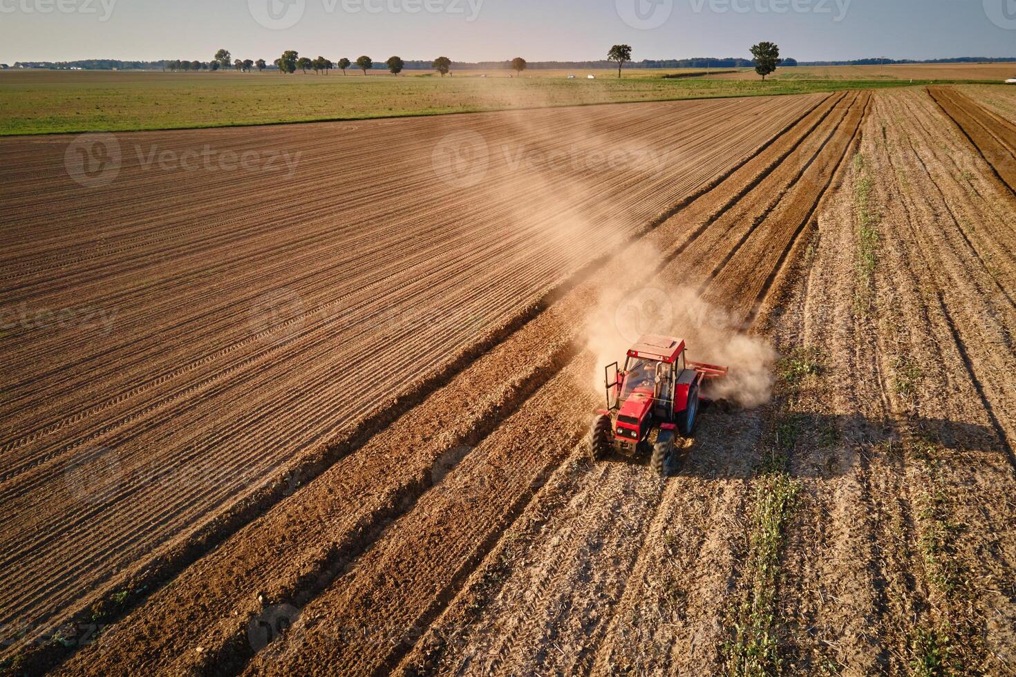 Red tractor working in agricultural field, cultivating and plowing dry soil, aerial view. Agribusiness concept. Small farming concept photo