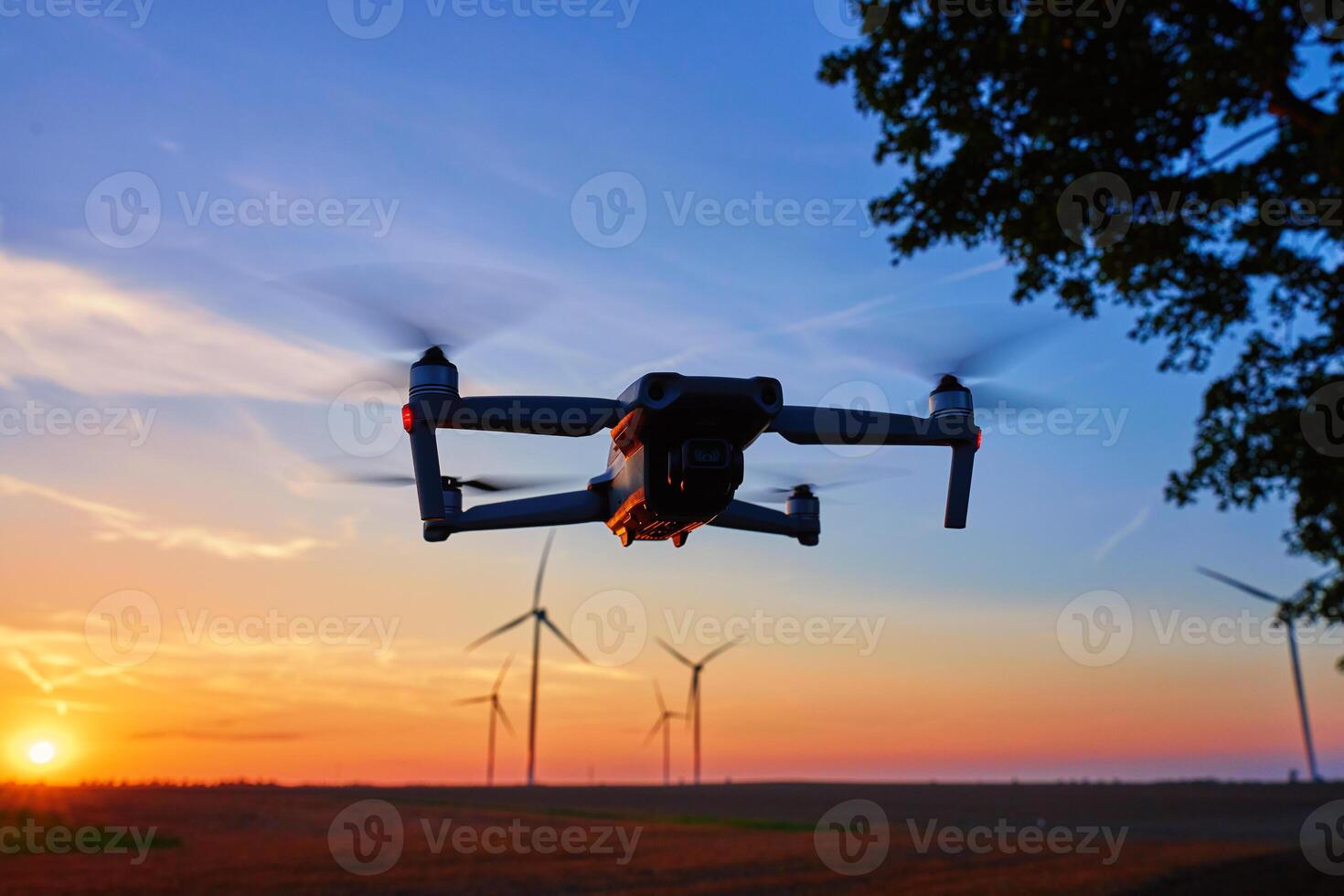 Drone in flight during sunset with wind turbines in background. Technology and sustainable energy concept photo