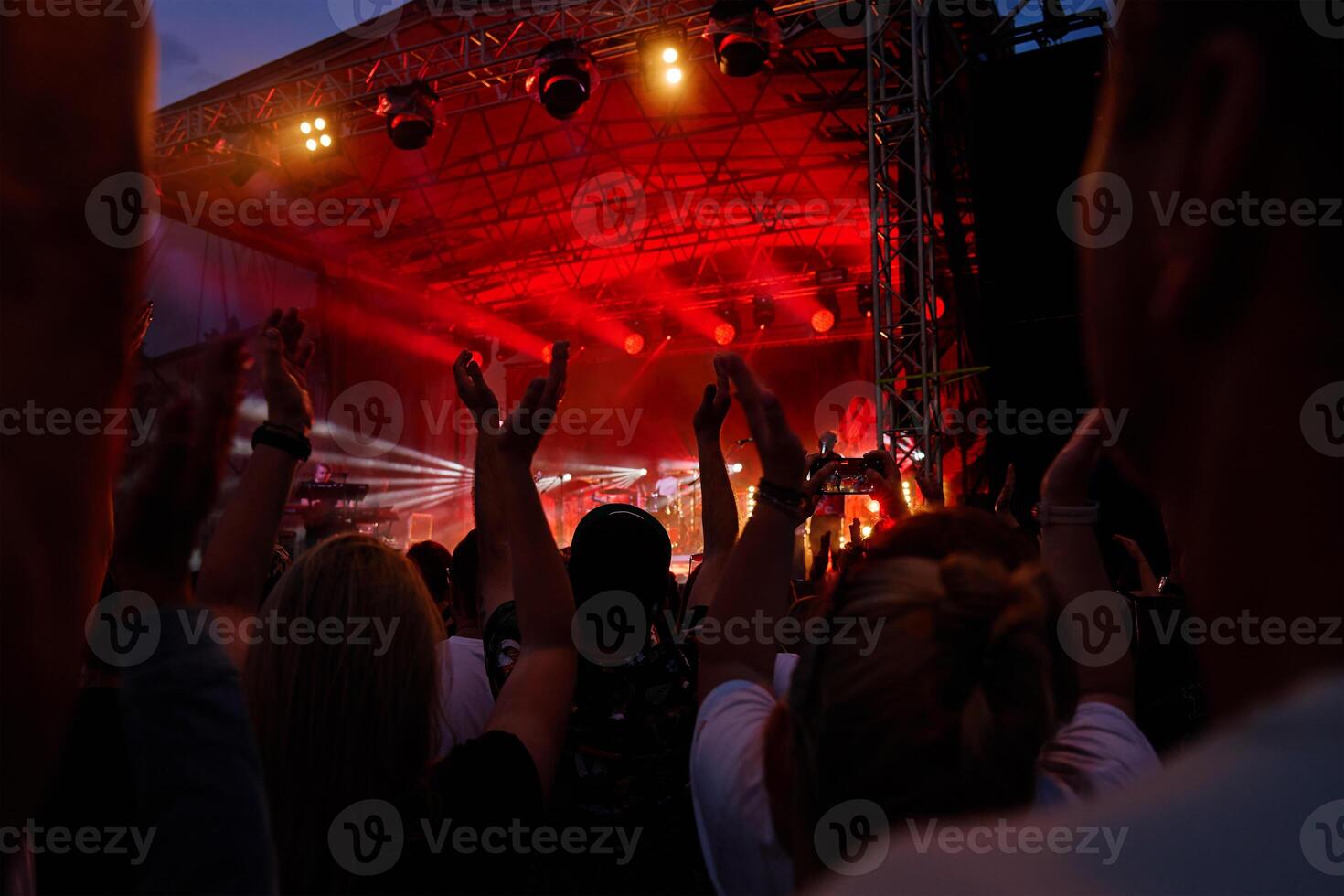 Silhouettes of crowd at concert in front of stage with bright spotlights. People enjoy live music at the band's performance. Concert hall with musicians on stage and fans during music festival photo