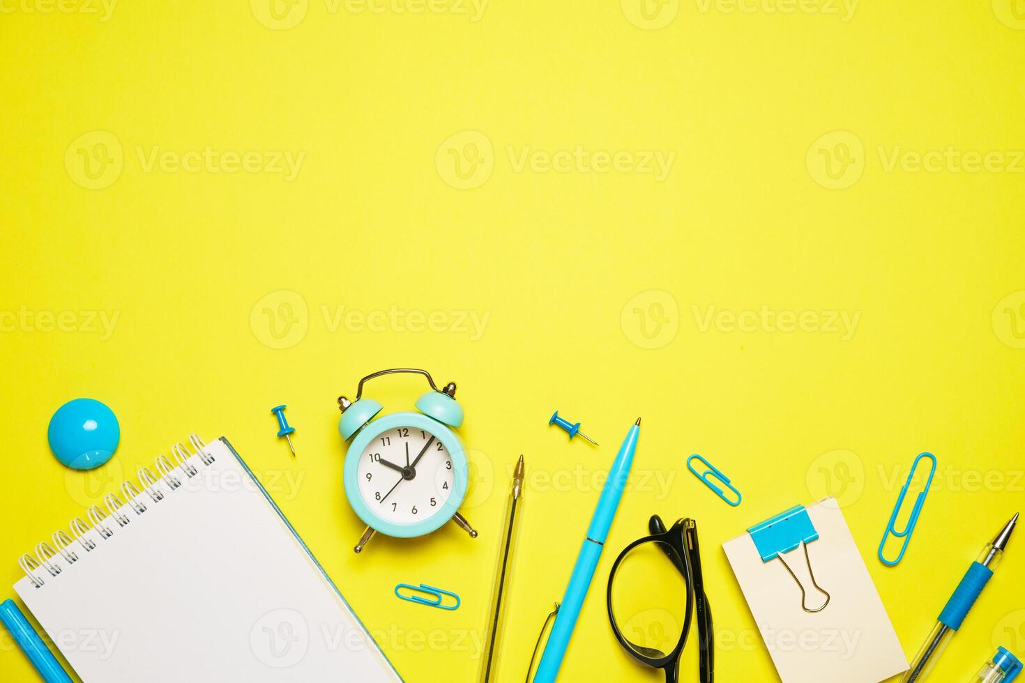 Notebook for writing pen and alarm clock with glasses on yellow background top photo