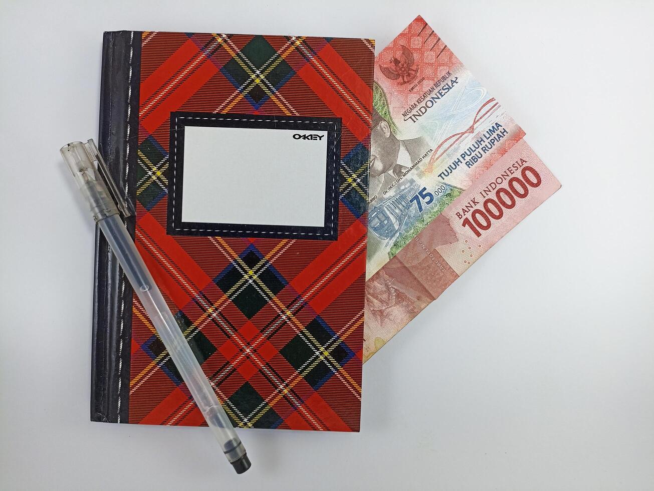 Wonosobo, Central Java Indonesia - August 9, 2024 Top view of pen, notebook and banknotes on white background. Indonesian Rupiah currency photo