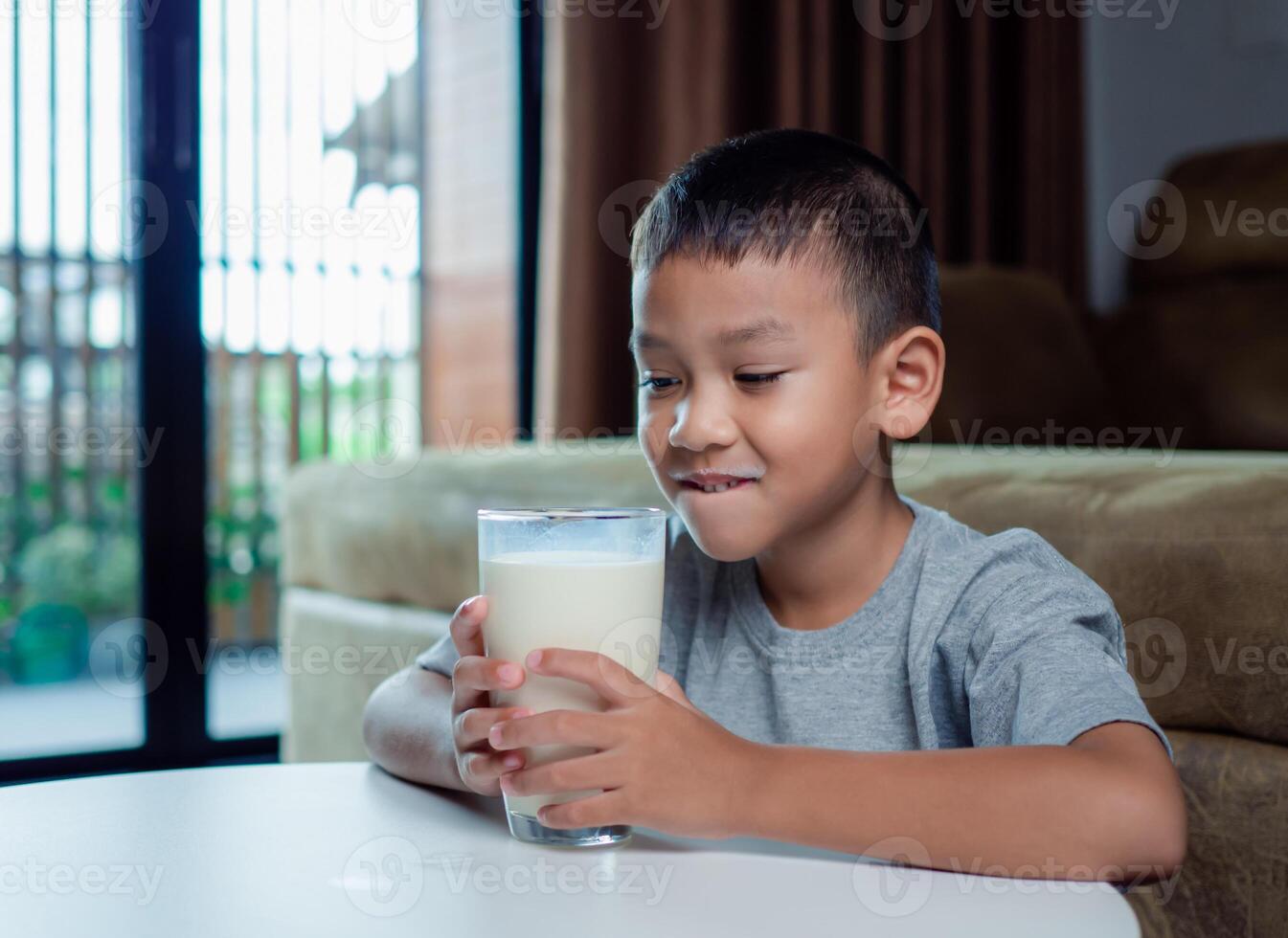 Portrait of a little young handsome kid boy in pink t-shirt, Concept of happy good nutrition, Holding a glass of milk on grey background, Smiling of Asian boy with a glass of milk. photo