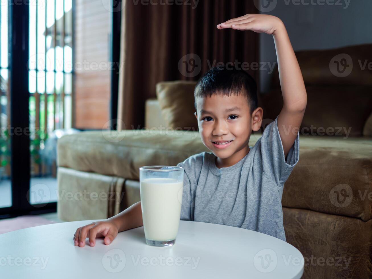 Concept of happy good nutrition, Portrait of a little young handsome kid boy in grey t-shirt, Show a glass of milk Inside a modern home background, Smiling of Asian boy with a glass of milk. photo