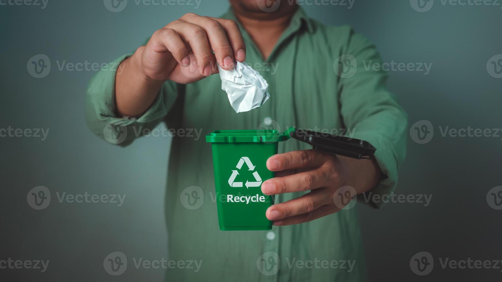 Man wearing a green shirt holding recycling bin and throw the paper in the bin, Waste sorting and sustainability concept, Recycle, Sustainable living and environmentally friendly habits concept. photo