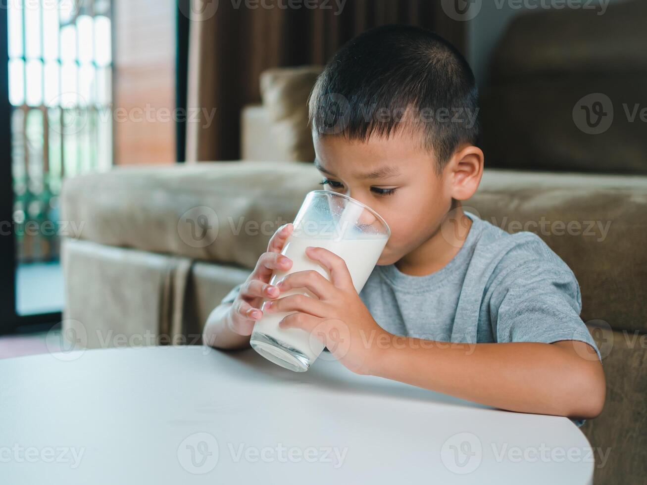 Portrait of a little young handsome kid boy in pink t-shirt, Concept of happy good nutrition, Holding a glass of milk on grey background, Smiling of Asian boy with a glass of milk. photo