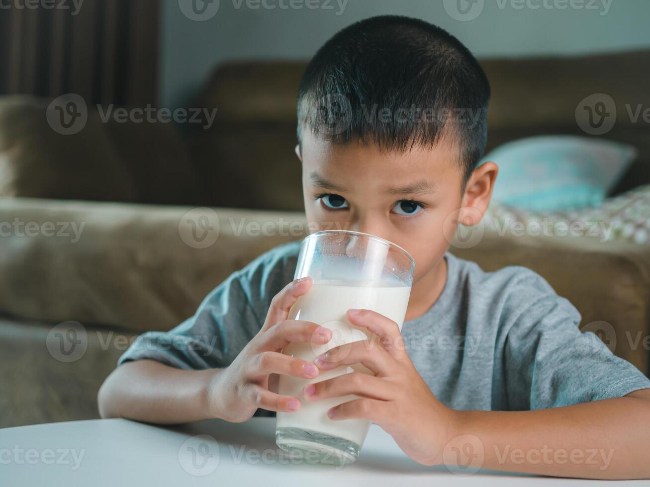 Portrait of a little young handsome kid boy in pink t-shirt, Concept of happy good nutrition, Holding a glass of milk on grey background, Smiling of Asian boy with a glass of milk. photo