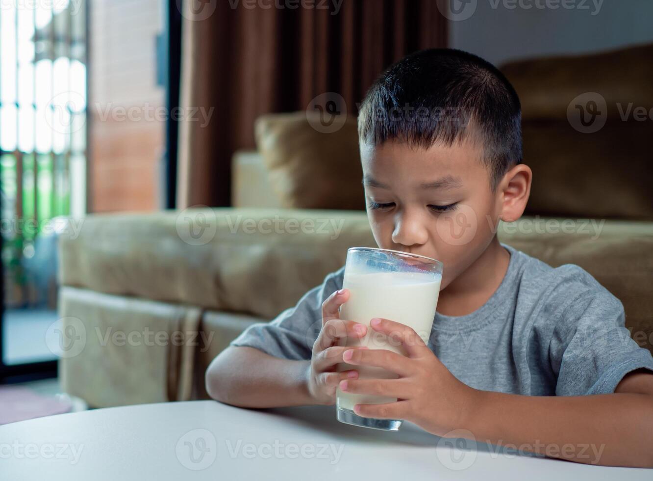 Portrait of a little young handsome kid boy in pink t-shirt, Concept of happy good nutrition, Holding a glass of milk on grey background, Smiling of Asian boy with a glass of milk. photo