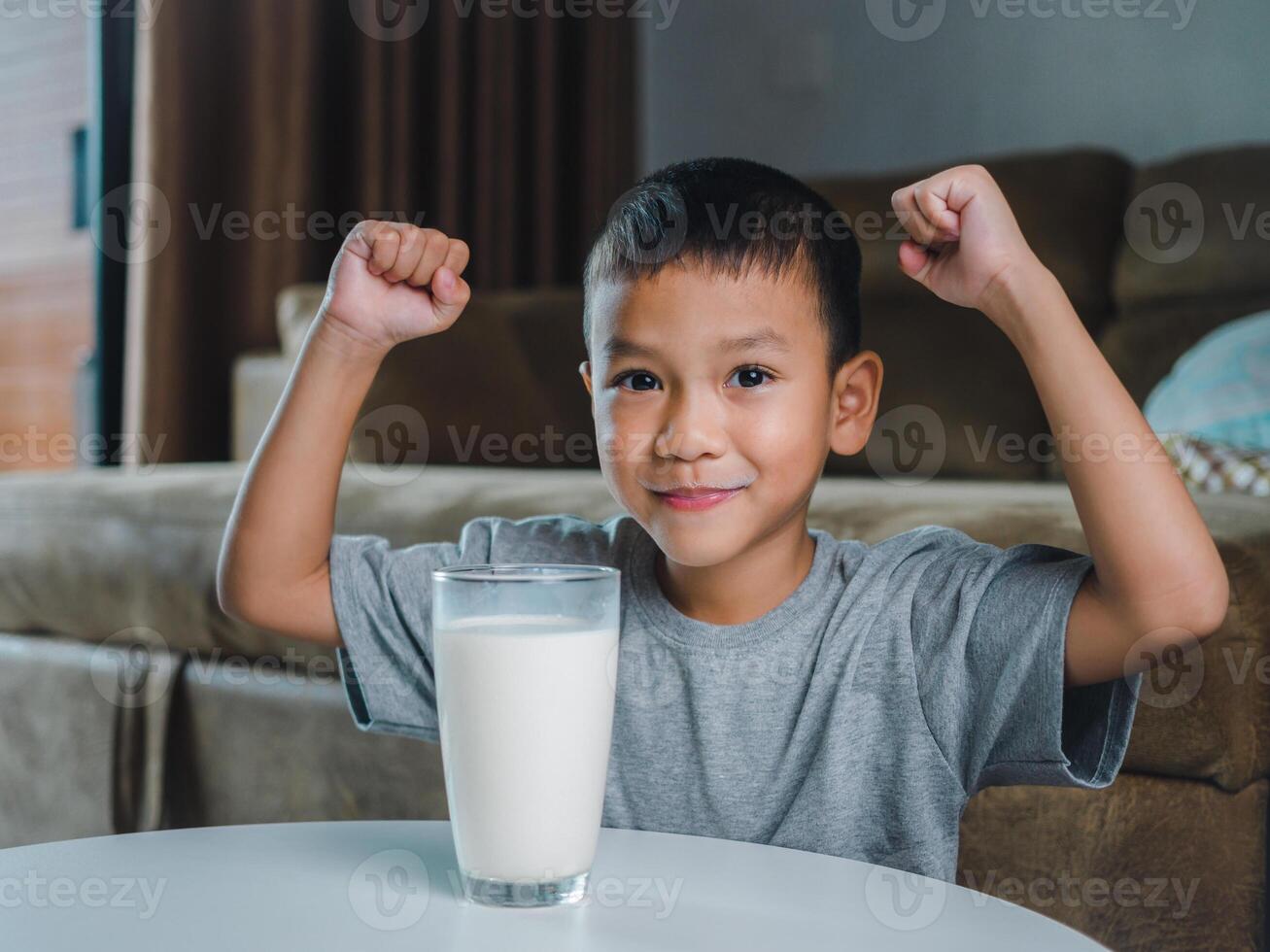 Concept of happy good nutrition, Portrait of a little young handsome kid boy in grey t-shirt, Show a glass of milk Inside a modern home background, Smiling of Asian boy with a glass of milk. photo