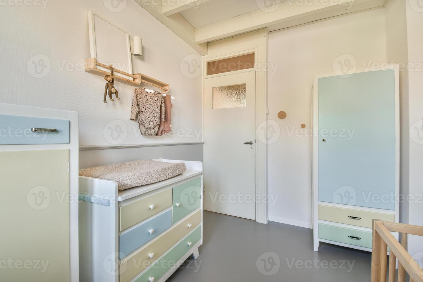 A small room with a dresser, a wardrobe and a baby's crib photo