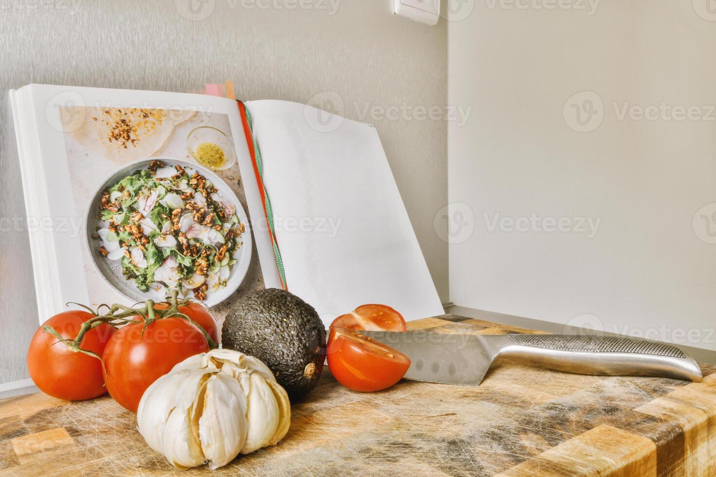 A book on a cutting board with tomatoes, garlic, and a knife photo