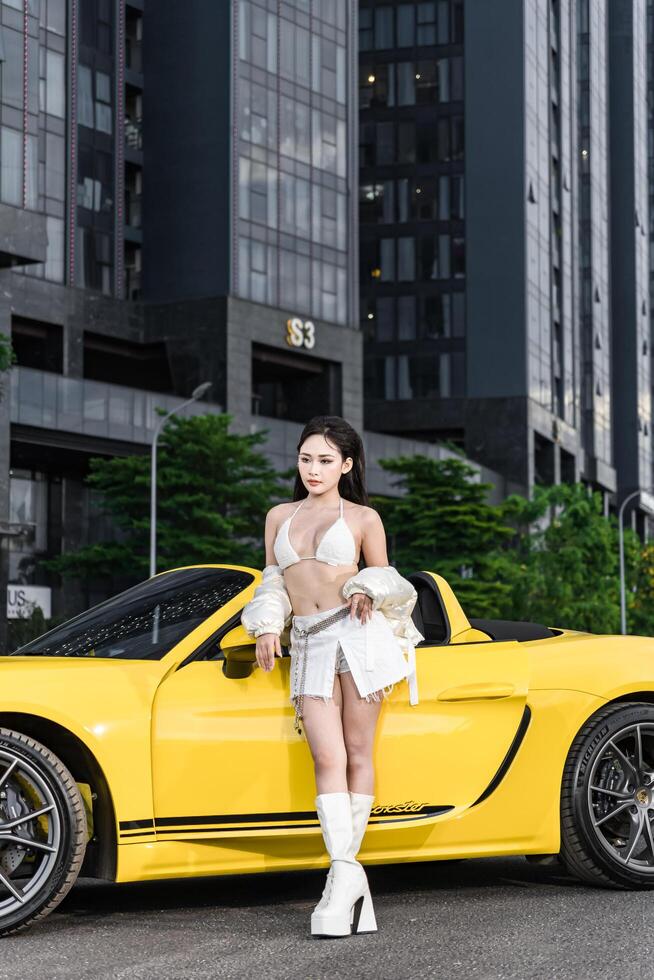 Hanoi, Vietnam - 26 Jun 2024 Beautiful young woman wearing bikini with Porsche 718 Boxster parked on the street during fashion photoshoot. photo