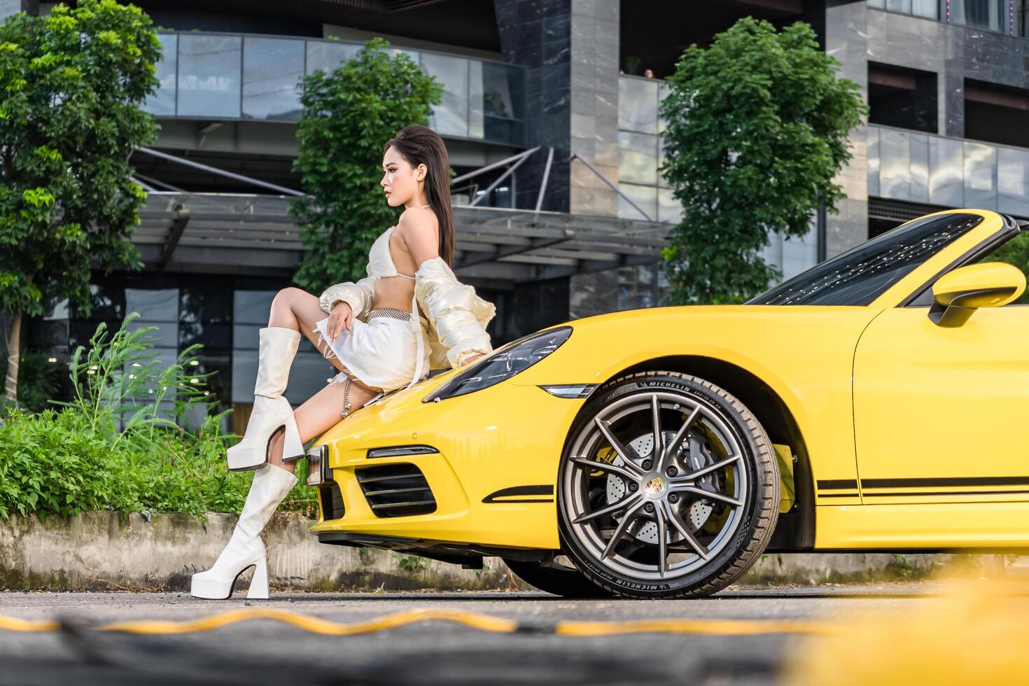 Hanoi, Vietnam - 26 Jun 2024 Beautiful young woman wearing bikini with Porsche 718 Boxster parked on the street during fashion photoshoot. photo