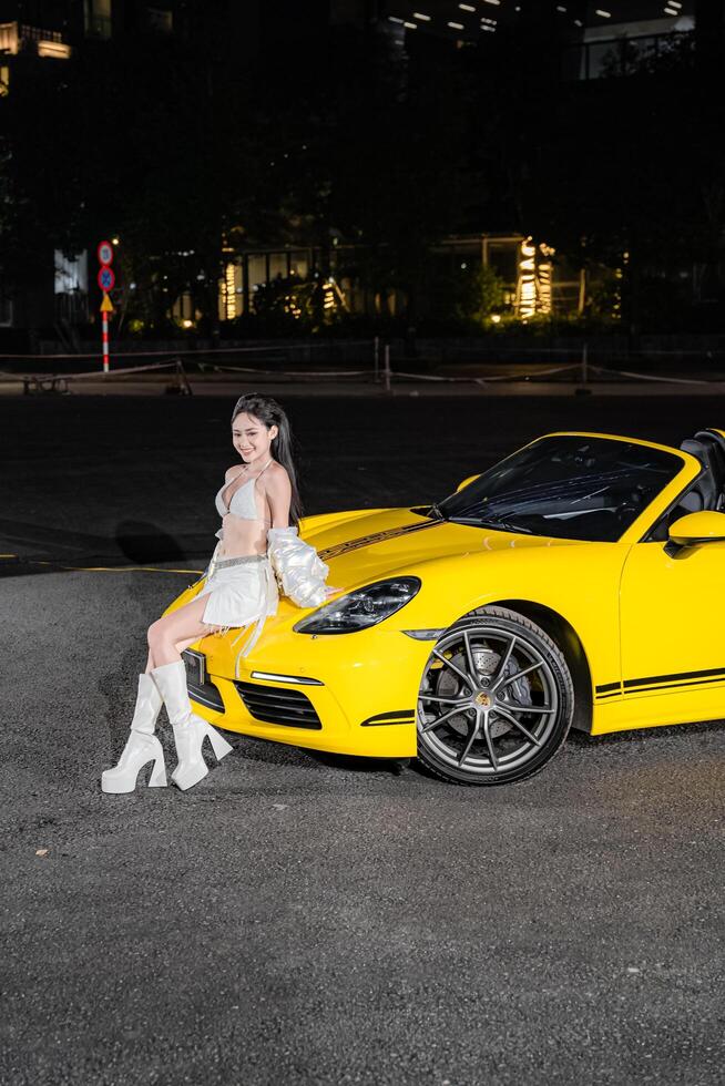 Hanoi, Vietnam - 26 Jun 2024 Beautiful young woman wearing bikini with Porsche 718 Boxster parked on the street during fashion photoshoot. photo