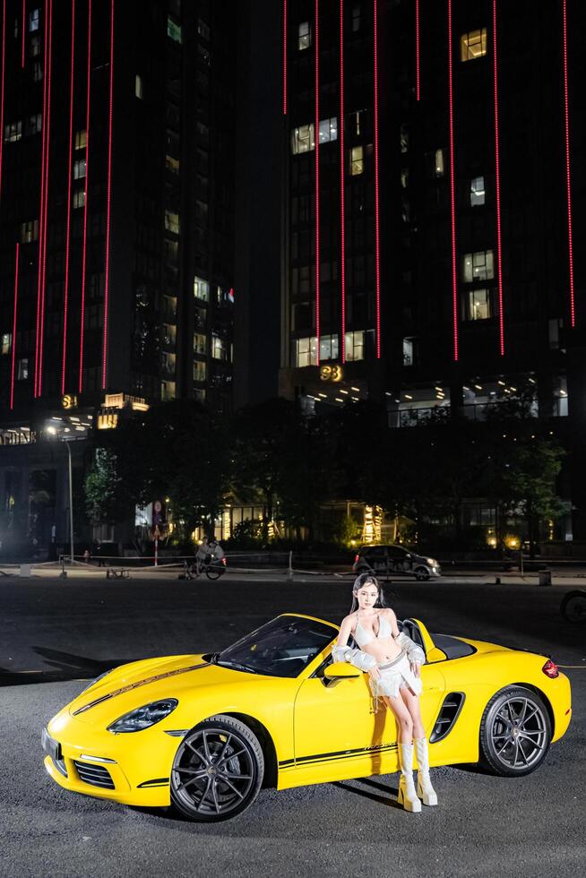 Hanoi, Vietnam - 26 Jun 2024 Beautiful young woman wearing bikini with Porsche 718 Boxster parked on the street during fashion photoshoot. photo
