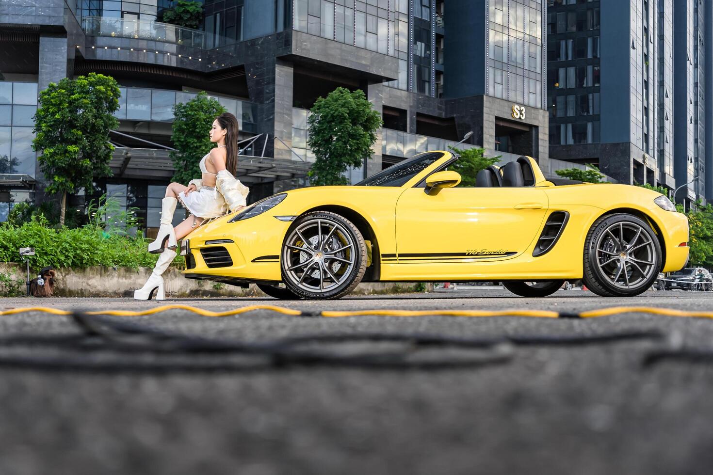 Hanoi, Vietnam - 26 Jun 2024 Beautiful young woman wearing bikini with Porsche 718 Boxster parked on the street during fashion photoshoot. photo