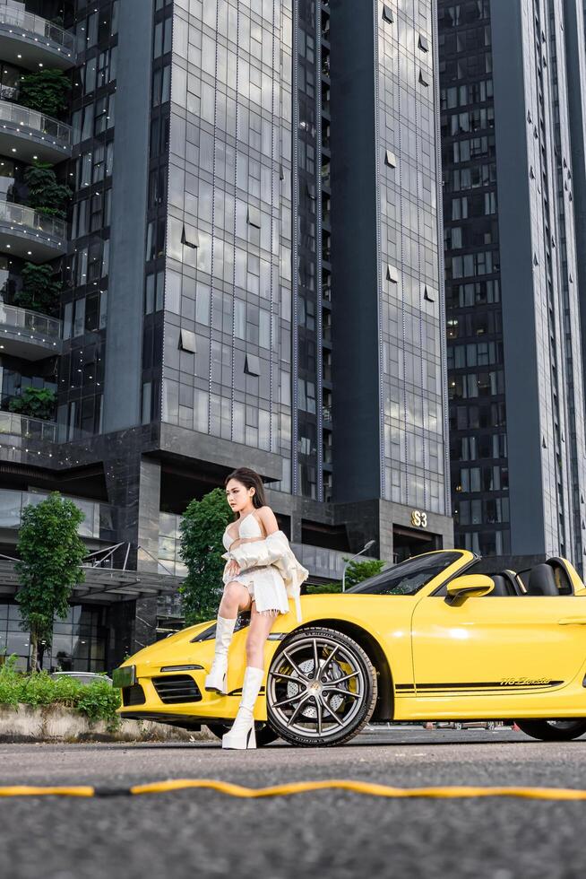 Hanoi, Vietnam - 26 Jun 2024 Beautiful young woman wearing bikini with Porsche 718 Boxster parked on the street during fashion photoshoot. photo