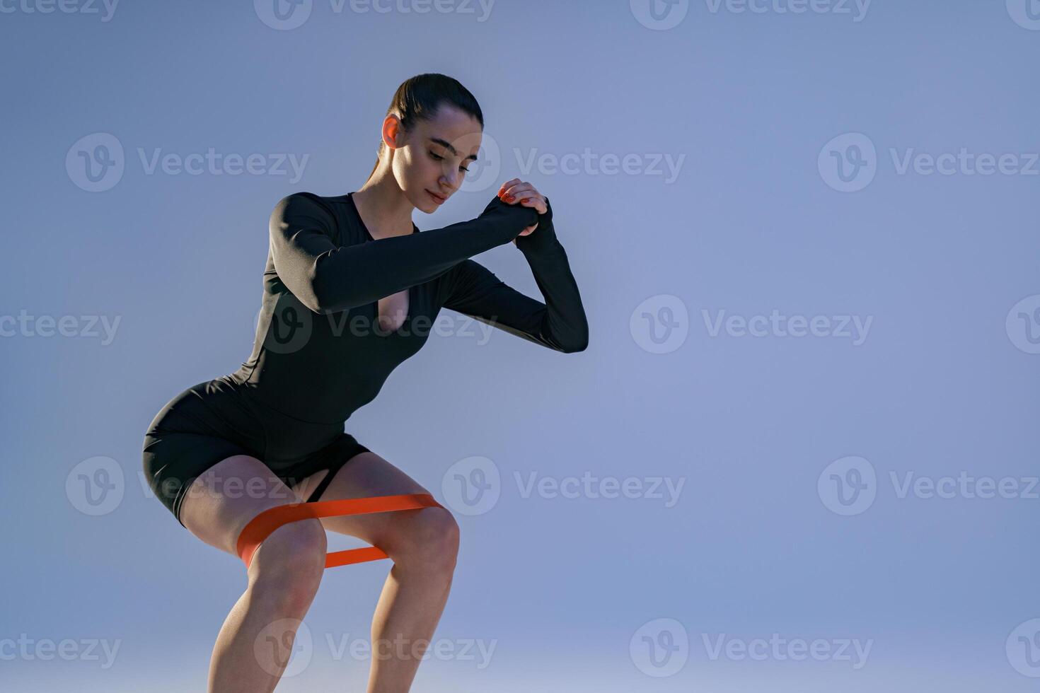 Attractive woman wearing sportswear trains legs with fitness elastic band on studio background photo