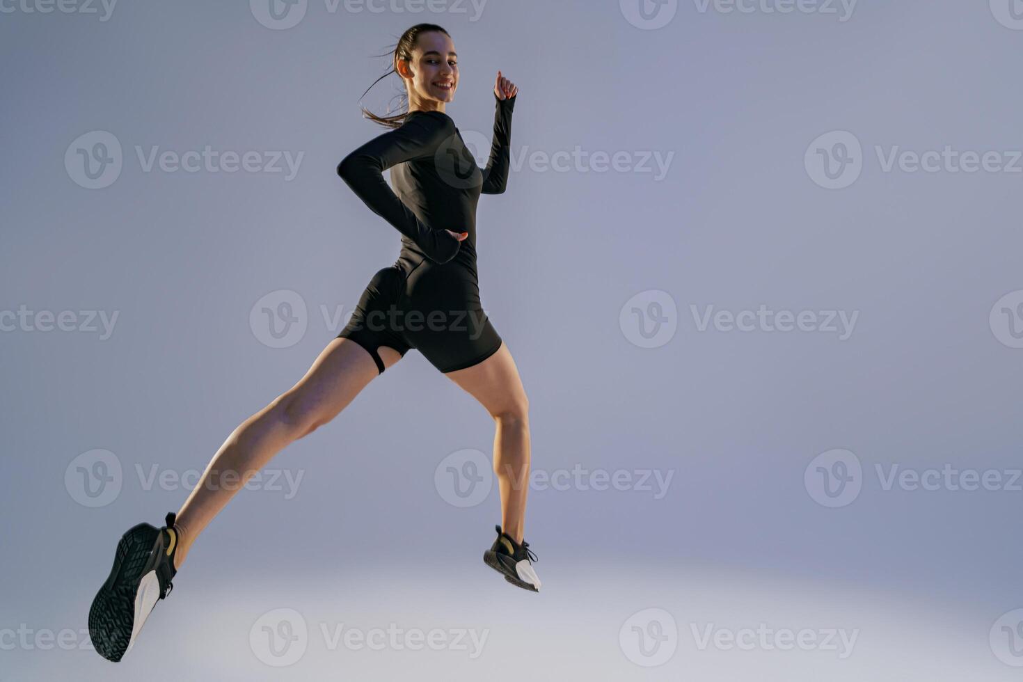 Smiling sporty woman running in Mid-Air exercising during cardio workout over studio background photo