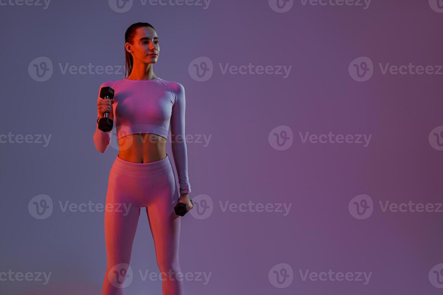 Attractive fitness woman doing exercises with dumbbells on studio background and looking at side photo