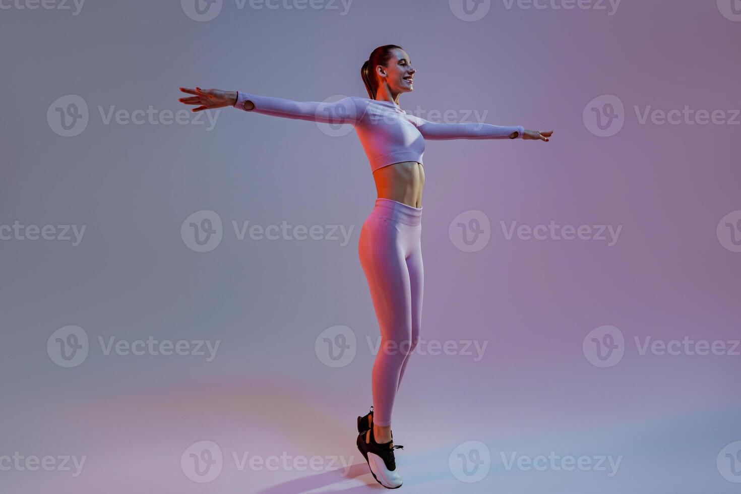 Happy sporty woman wearing sportswear stand with raised up arms on studio background photo