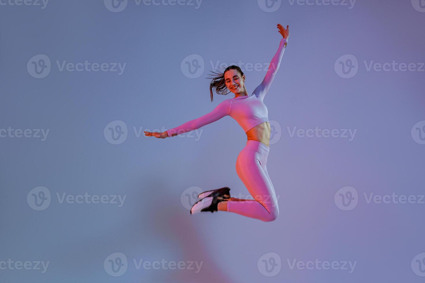 Smiling sporty woman in sportswear jumping on studio background. Sport and healthy lifestyle photo