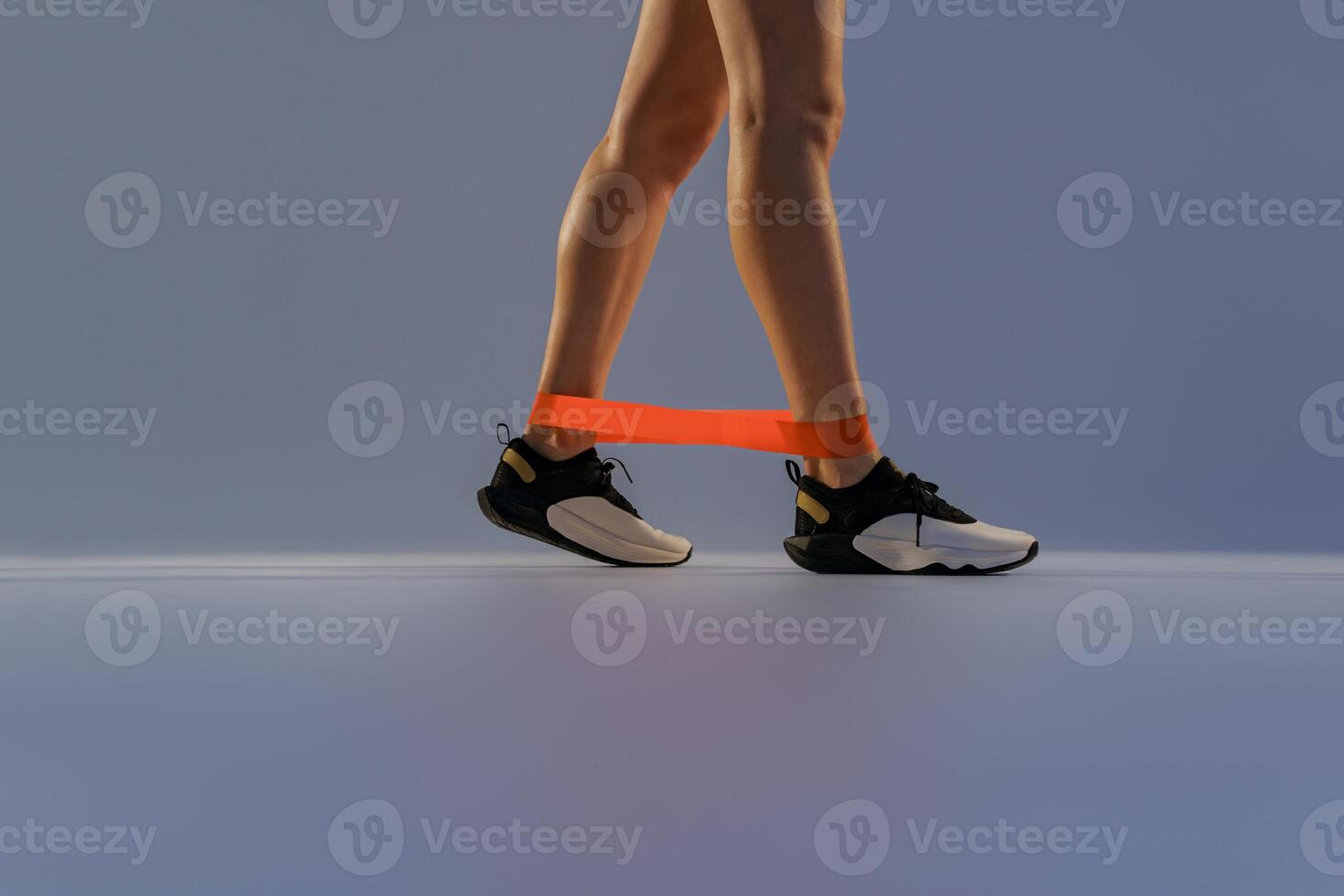 Close up of woman wearing sportswear trains legs with fitness elastic band on studio background photo