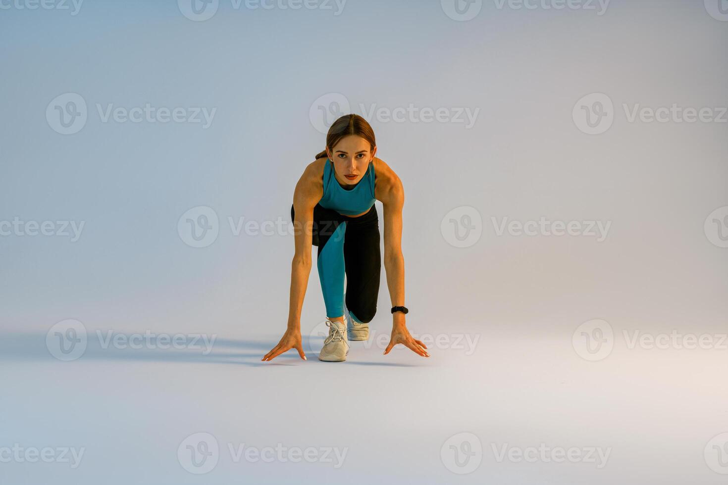 Female athlete in starting position ready for running looking at camera on studio background photo